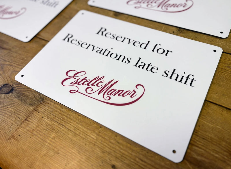 White reserved staff parking sign with burgundy Estelle Manor branding and corner fixing holes