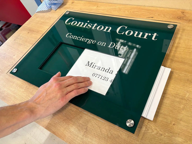Green Coniston Court concierge on duty sign with a paper insert sliding into the display window