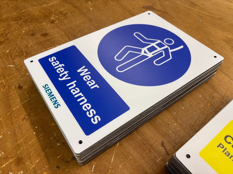 Stack of blue and white Wear safety harness signs with Siemens branding